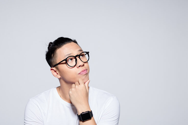 Pensive asian man wearing glasses and a white tshirt against a white background