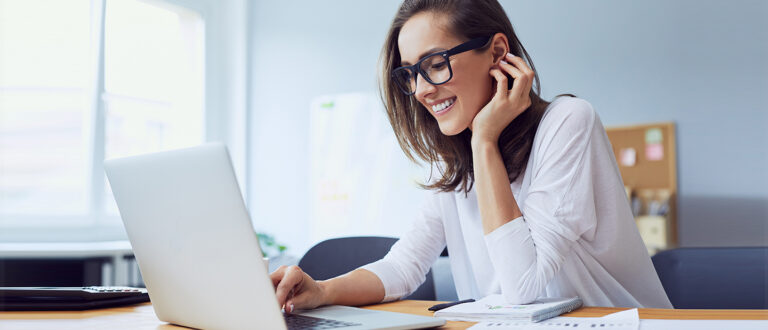 Smiling woman wearing glasses, working from home at her laptop