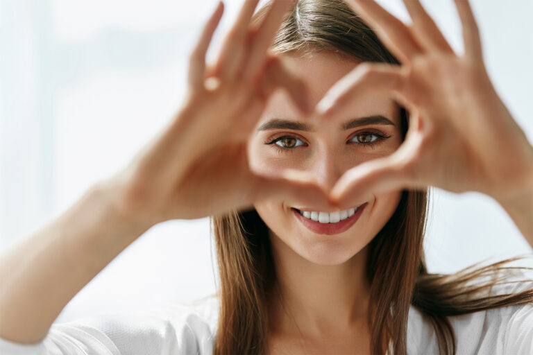 young woman smiling and making a heart shape with her hands in front of her eyes