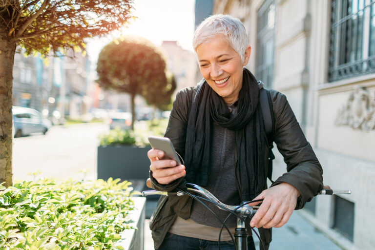 Woman leaning on a bike outside looking at her phone smiling